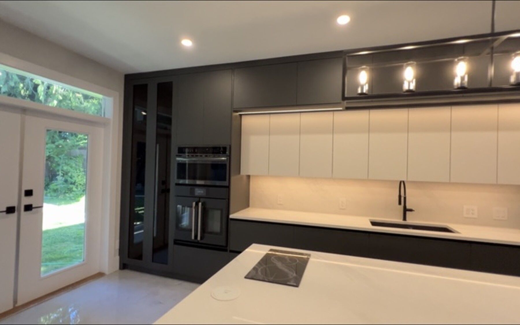 The completed kitchen looking toward the garden doors, with under-cabinet lighting and the wall ovens integrated into the tall run