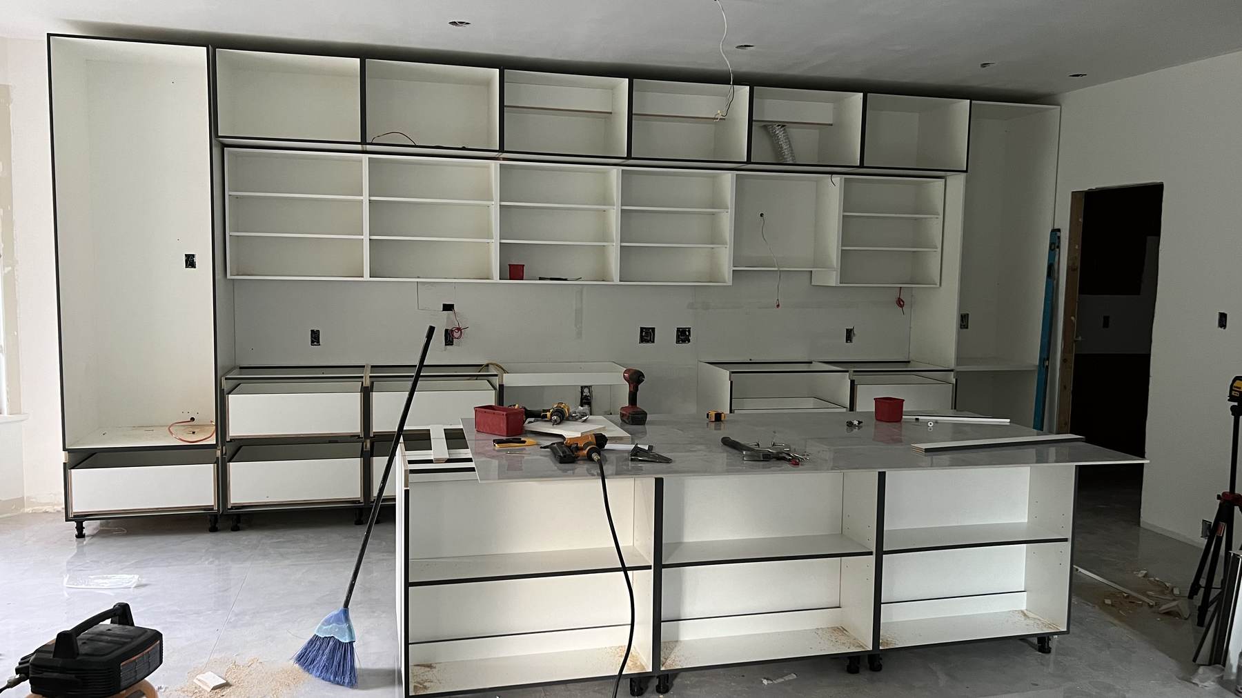 White custom cabinet carcasses installed along the kitchen wall with the island frame set in the centre of the room