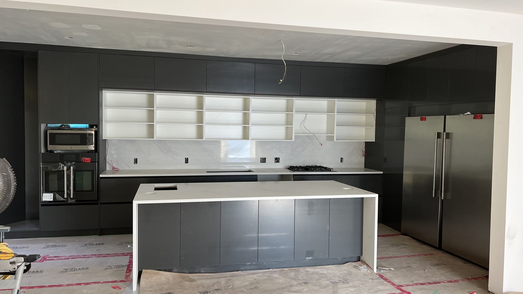 Dark handleless cabinet fronts installed with the island in place and integrated appliances in the tall run