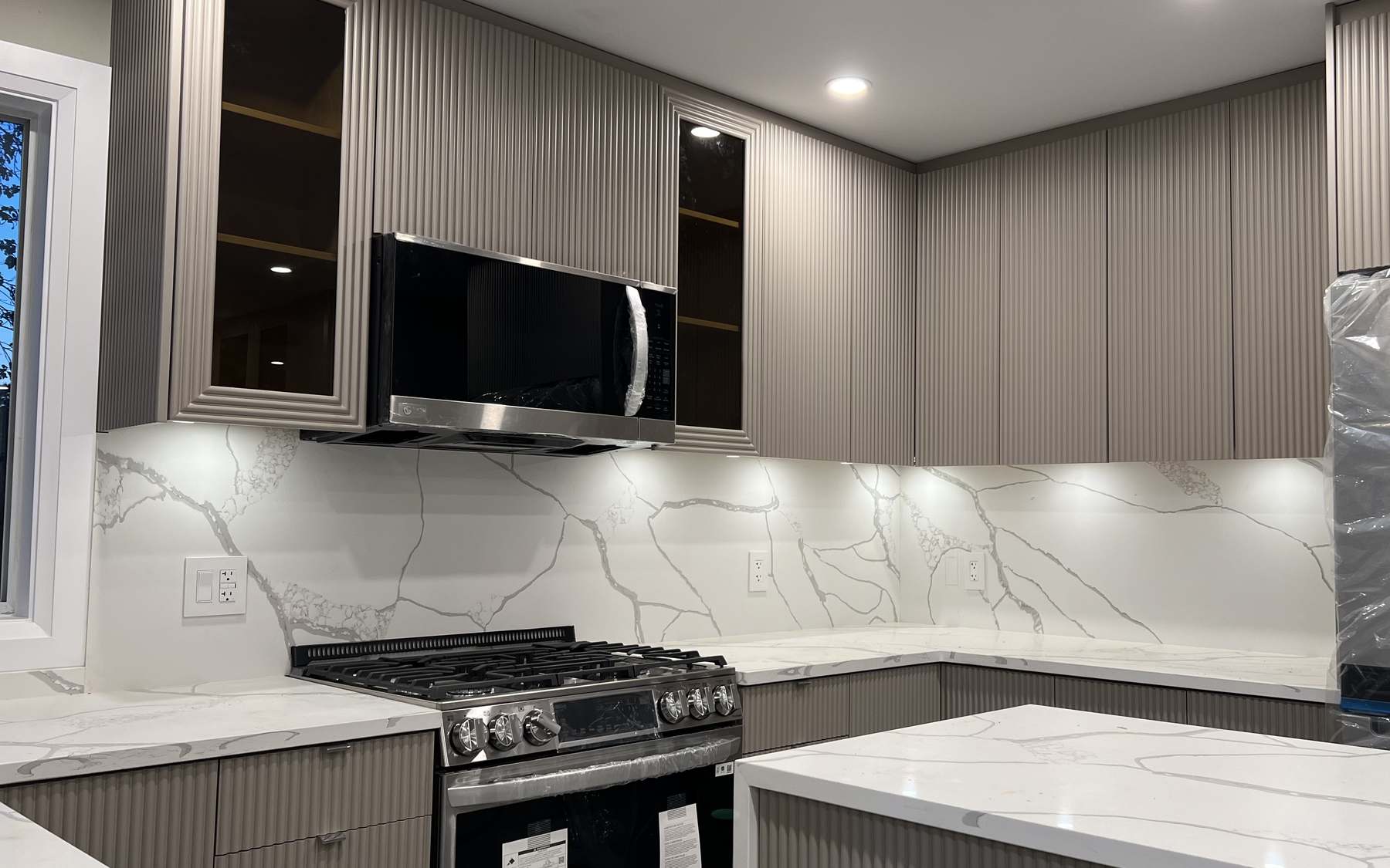 Finished Coquitlam kitchen detail: fluted cabinetry, integrated microwave and the veining in the slab backsplash