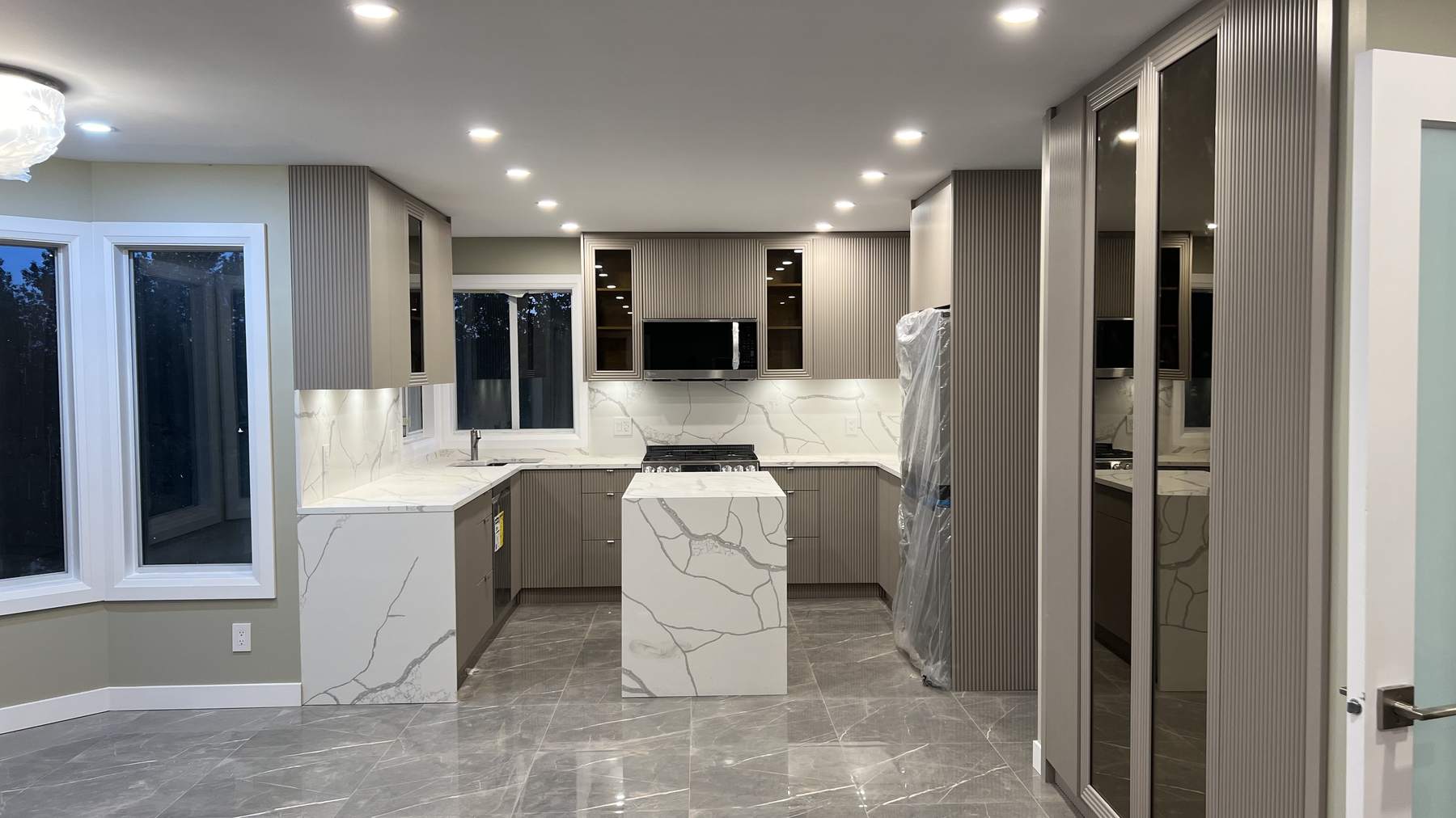 The completed kitchen at night, with warm integrated lighting across the full U-shaped layout and the waterfall island