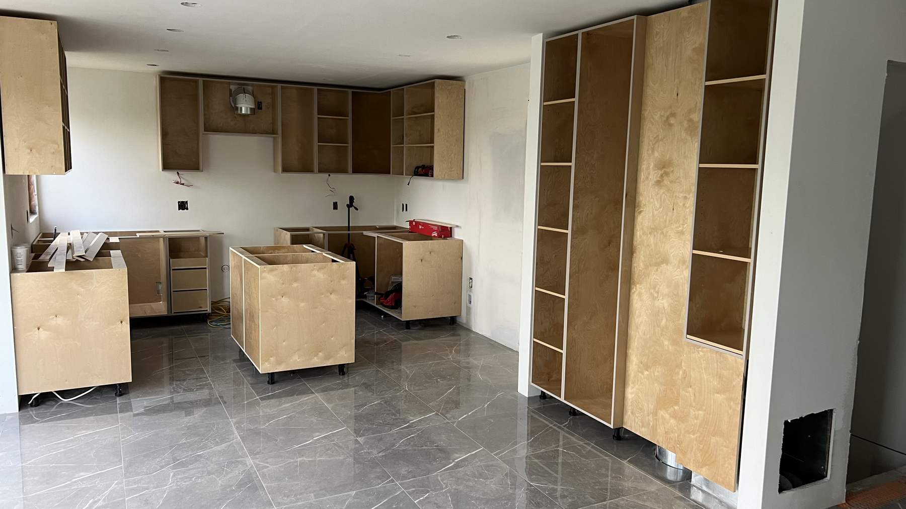 Raw plywood cabinet carcasses installed around the kitchen, with the island box and a full-height pantry run in place