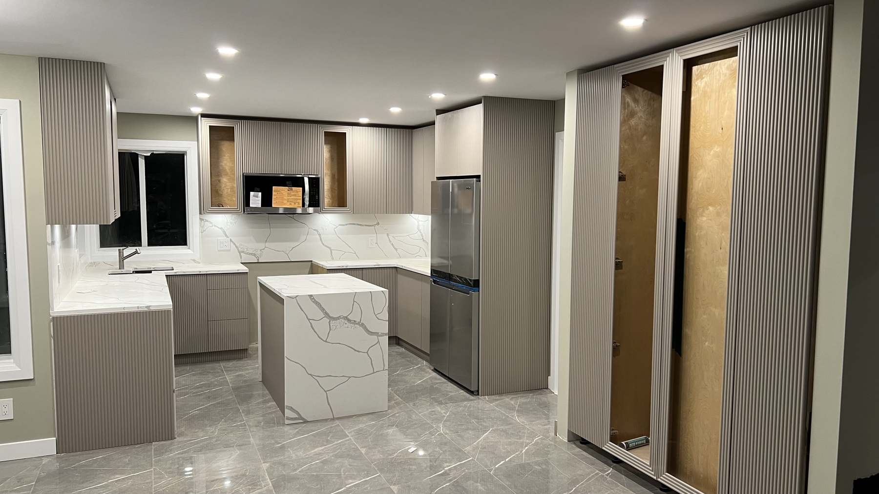 Taupe cabinet fronts and fluted panelling installed, with appliances set and the waterfall island complete