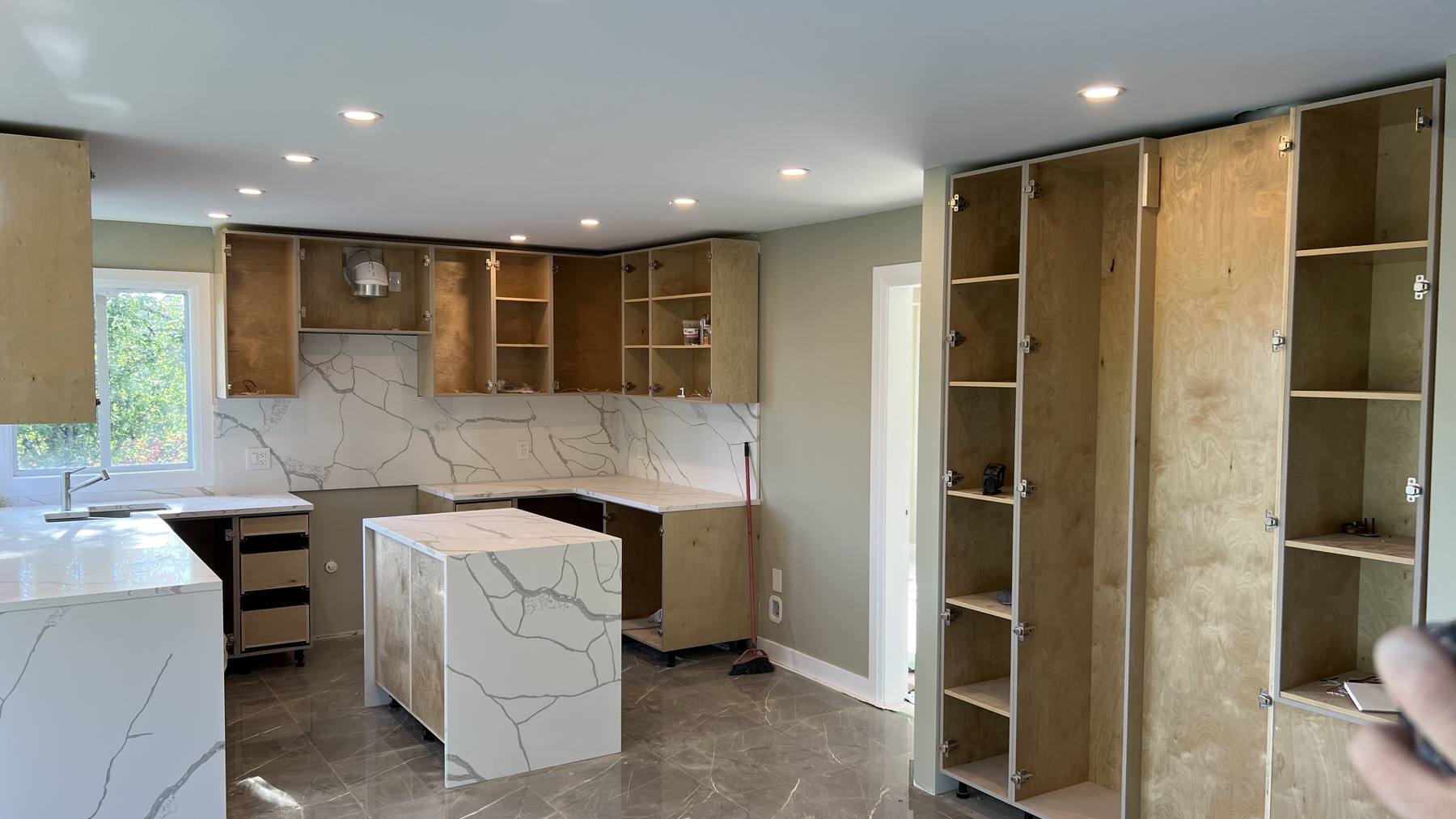 Quartz countertops and a full-height slab backsplash installed, with the waterfall island edge set and cabinet boxes still open